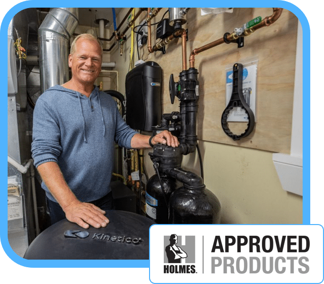 A smiling man standing next to a Kinetico water filtration system in a utility room, with a 