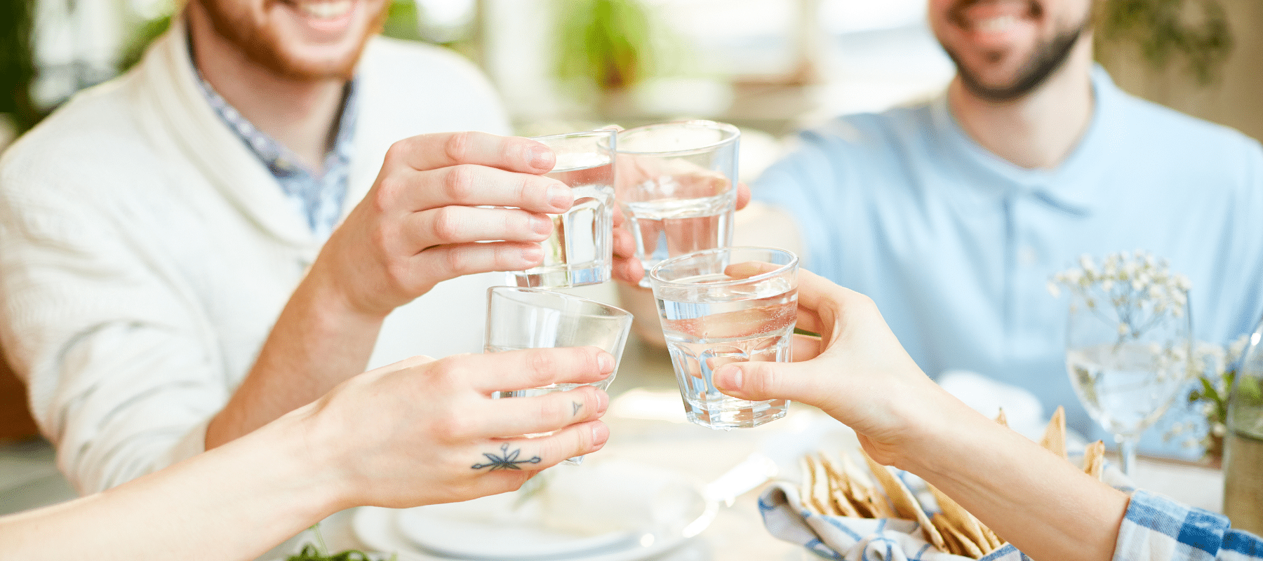 Friends raising glasses of water in a toast at a dining table