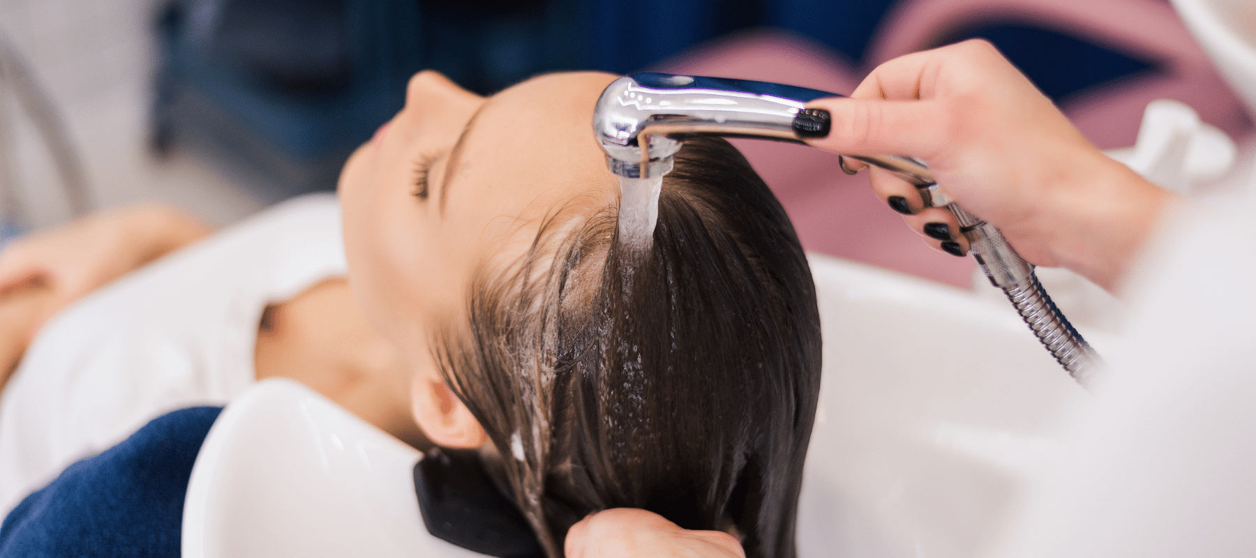 A hairstylist washing a client's hair with a handheld sink sprayer
