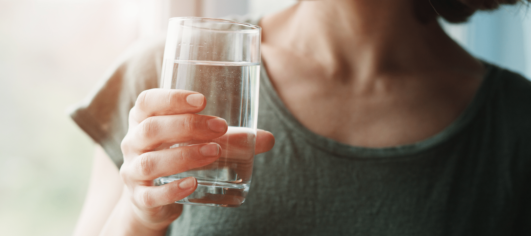 A woman holding a glass of water near a window with soft lighting