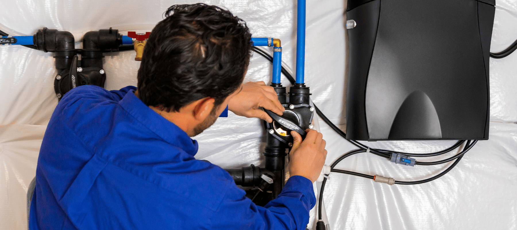 A technician in a blue uniform installing a Kinetico water filtration system