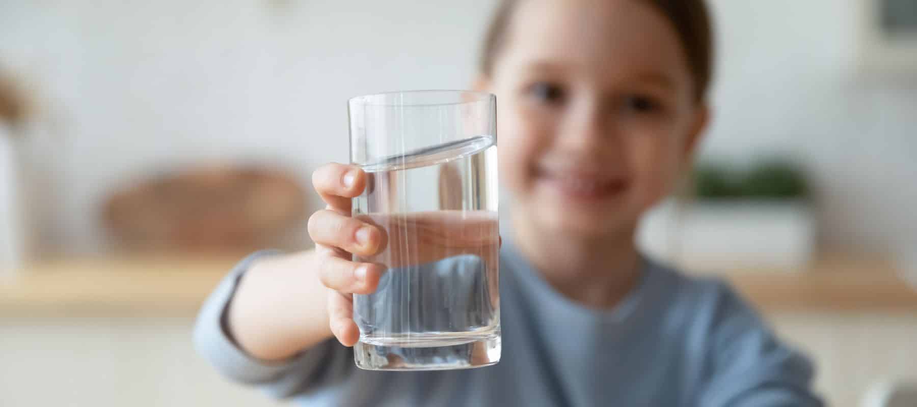 A smiling child holding out a glass of clear water