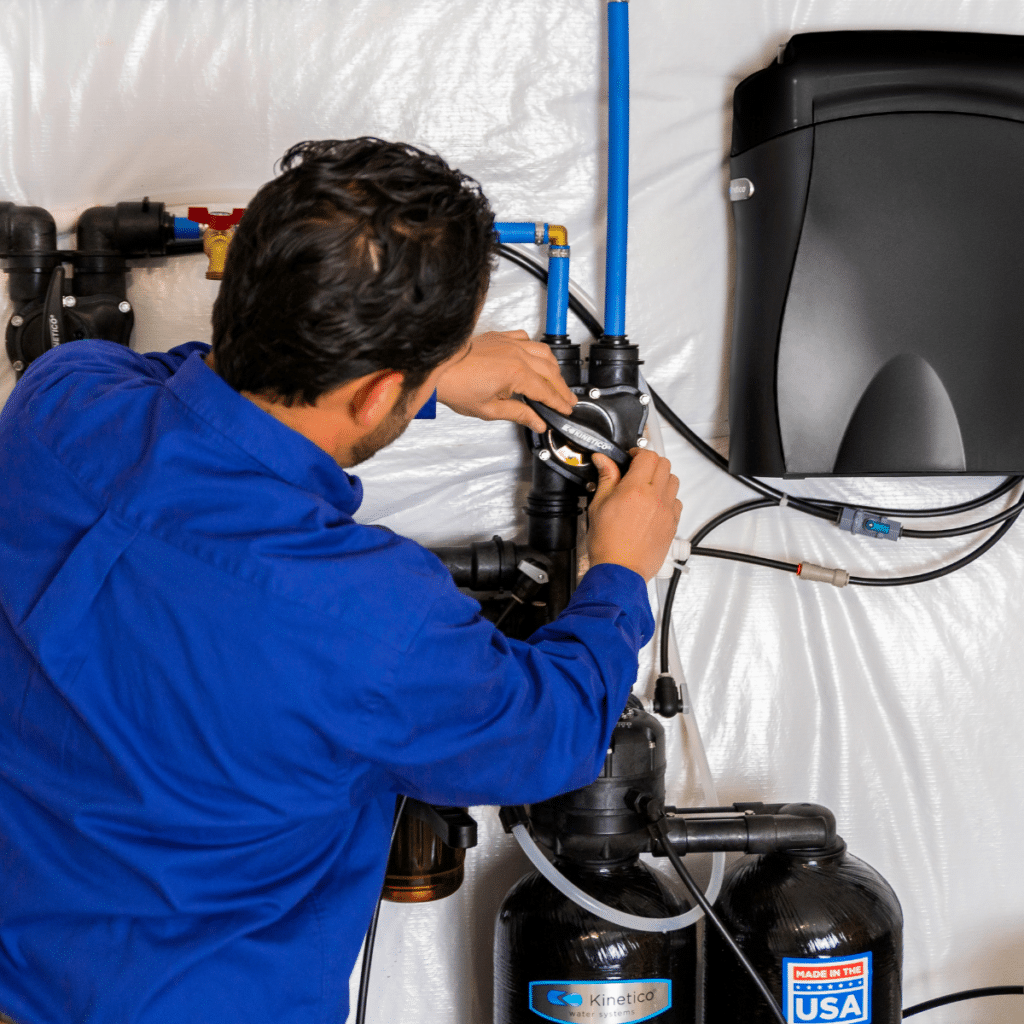 A technician in a blue uniform installing a Kinetico water filtration system