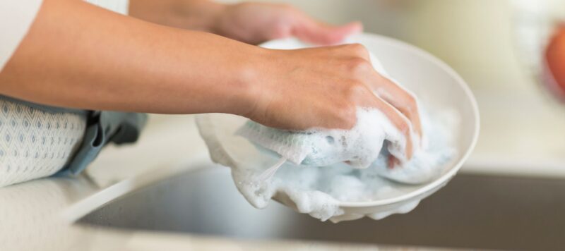 closeup of someone washing a plate with a soapy wash rag
